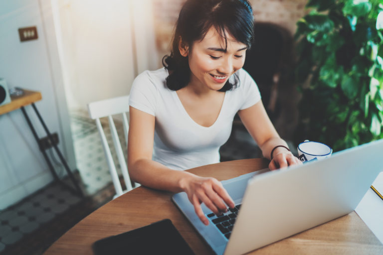Top view of smiling Asian woman working on laptop while spending time at home.Concept young modern people using mobile devices.Blurred background, flares effect